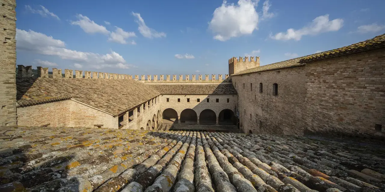 Cortile interno di un castello a Tolentino, Marche, con tetti in cotto e cielo azzurro.