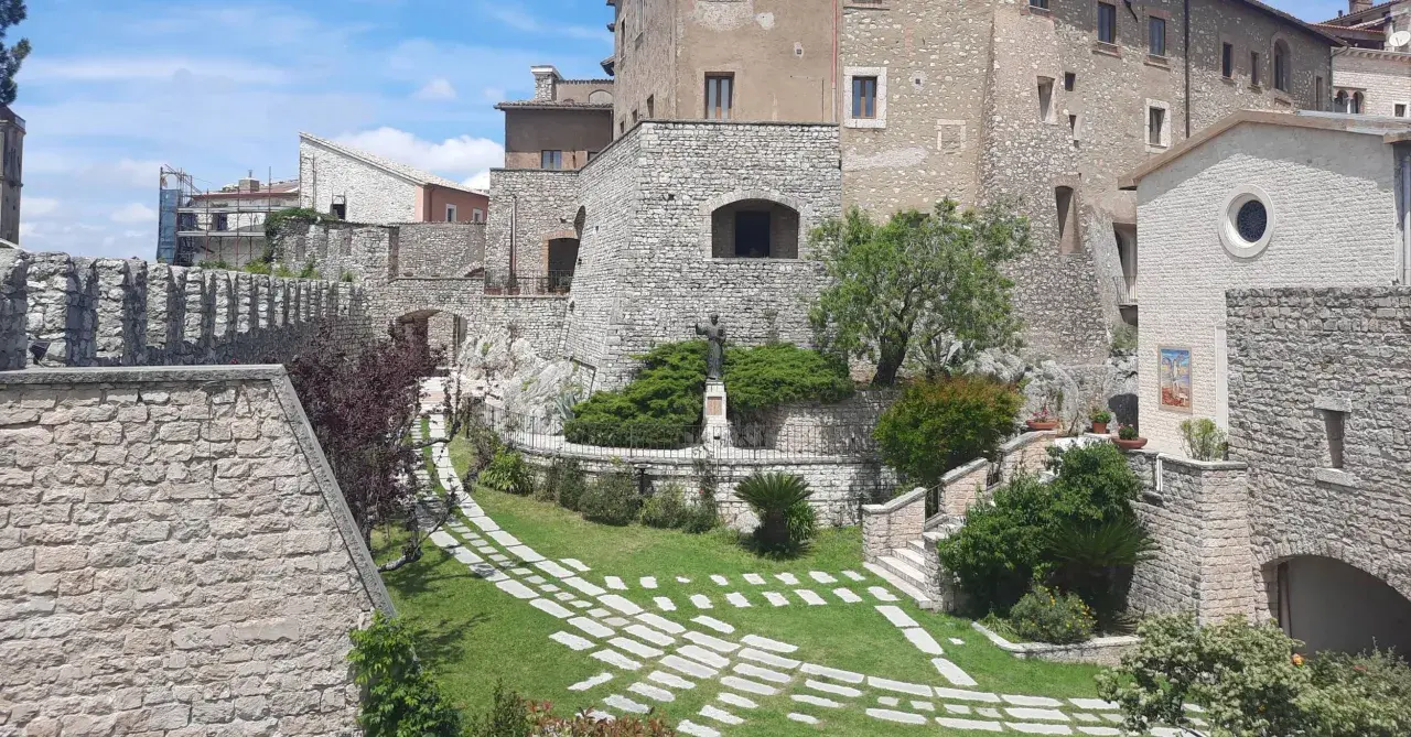 Un angolo suggestivo del centro storico di Rieti, con antiche mura in pietra, un giardino curato e una statua.