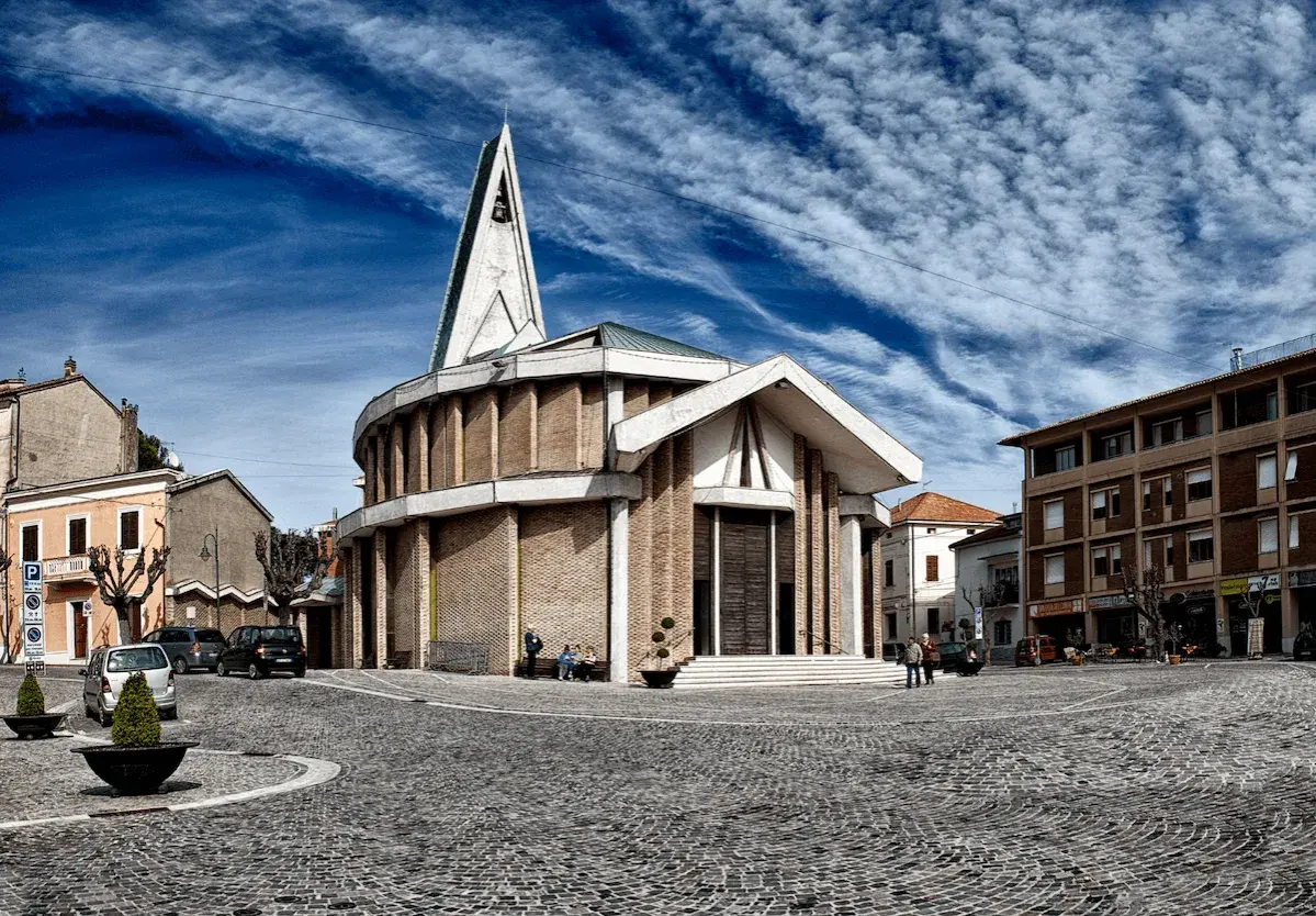 Piazza del centro di Numana con una chiesa moderna, cielo blu e nuvole bianche.
