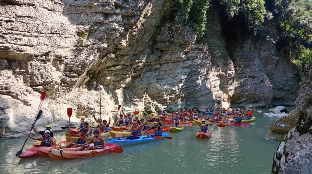 Gente in kayak esplora un canyon con pareti rocciose imponenti, simili a marmitte dei giganti nelle Marche.