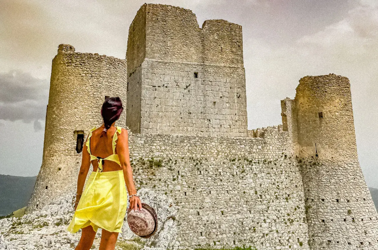 Donna in abito giallo ammira la Rocca Calascio, un luogo da non perdere per la sua storia e panorami mozzafiato.