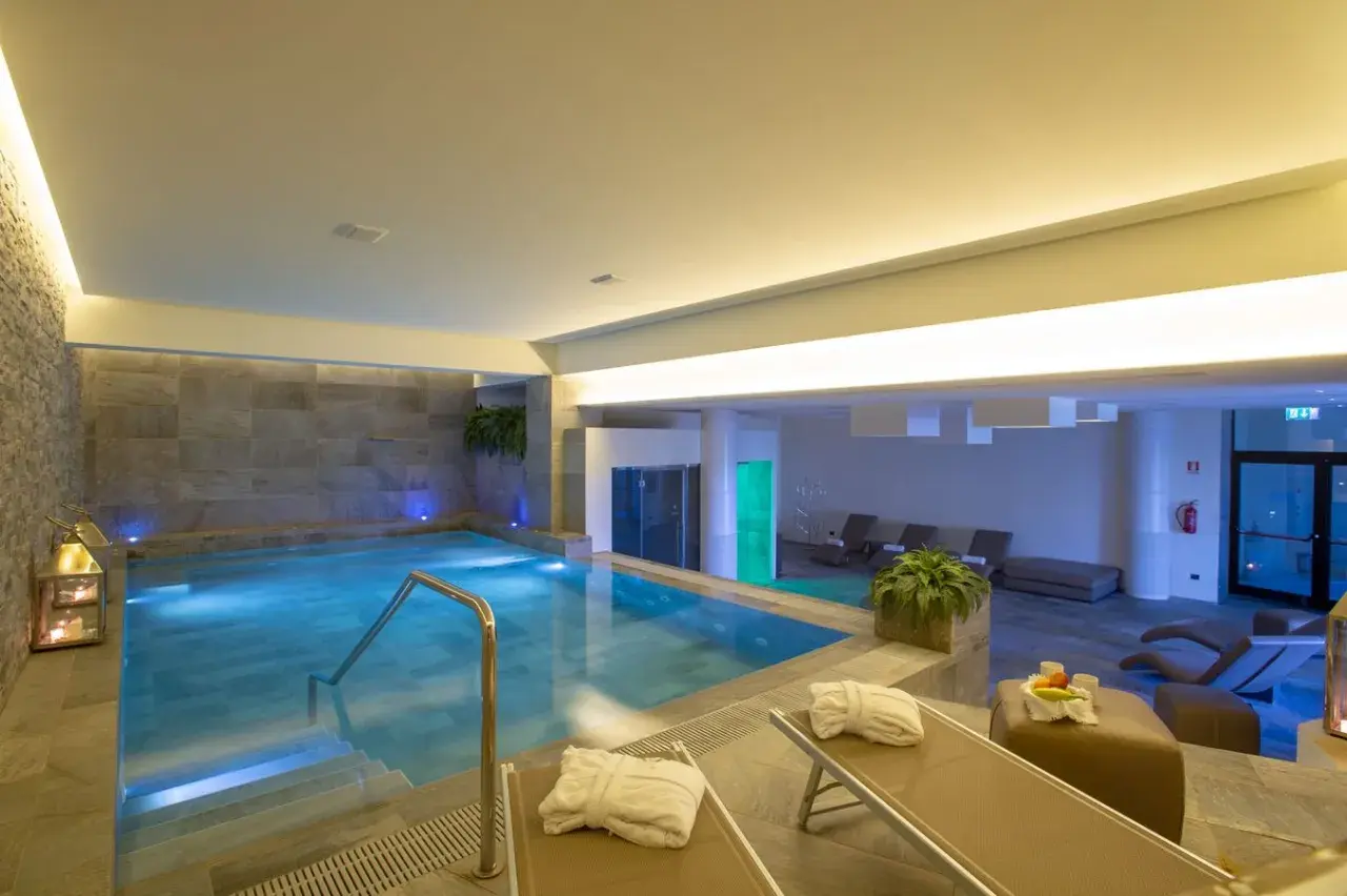 Piscina interna illuminata con luci blu, lettini prendisole con accappatoi, piante e lanterne. Un'oasi di relax in una spa nelle Marche.