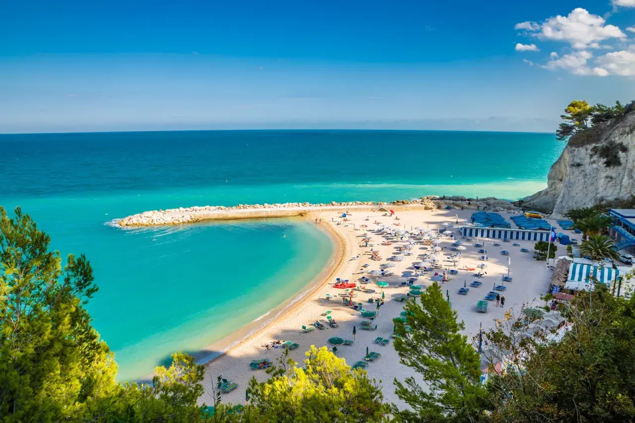 Spiagge Sirolo con acque turchesi, sabbia dorata, ombrelloni e gente che si gode il sole.