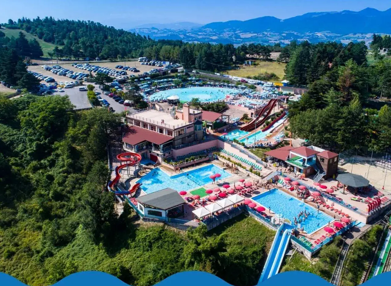 Vasta area con piscine, scivoli e ombrelloni rossi, immersa nel verde delle colline. Un divertente parco acquatico nelle Marche per tutta la famiglia.