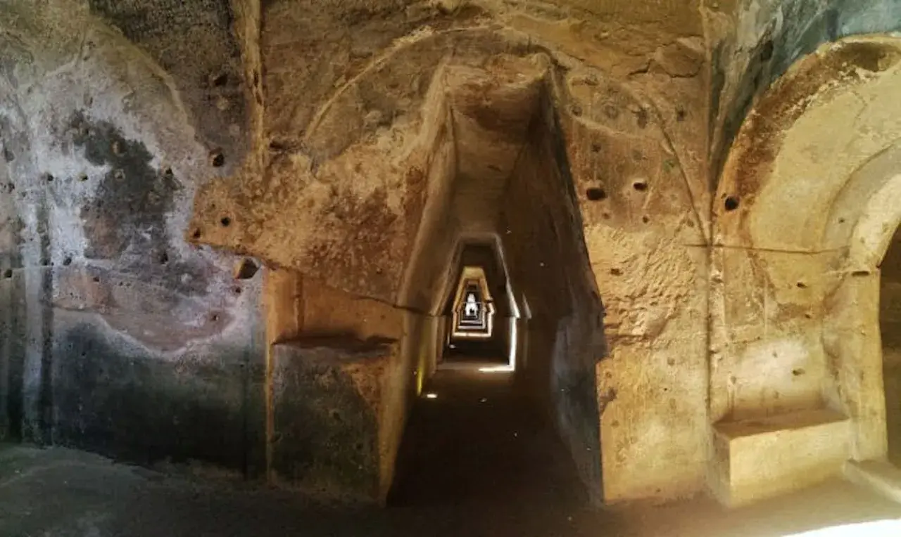 Interno della grotta della Sibilla: un corridoio stretto e trapezoidale scavato nella roccia, con nicchie e aperture.