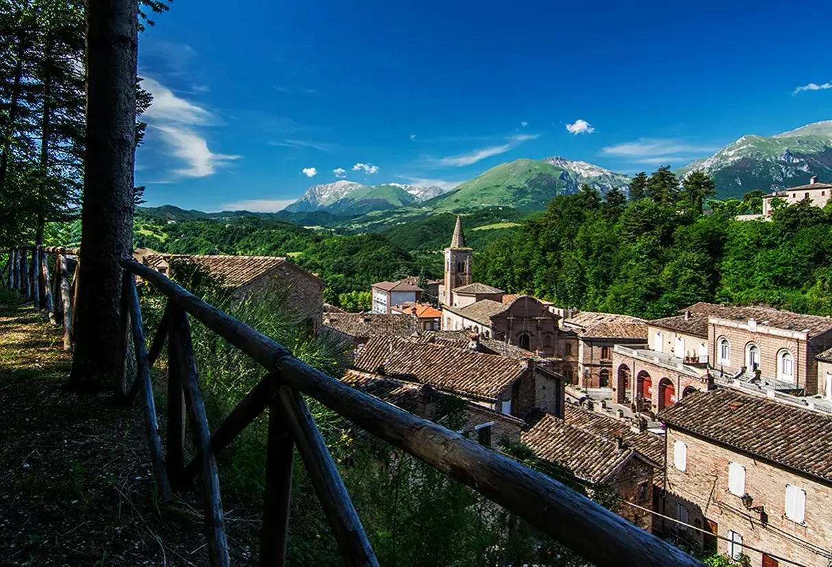 Borgo incantevole tra i **Monti Sibillini**, con tetti in cotto e montagne sullo sfondo.