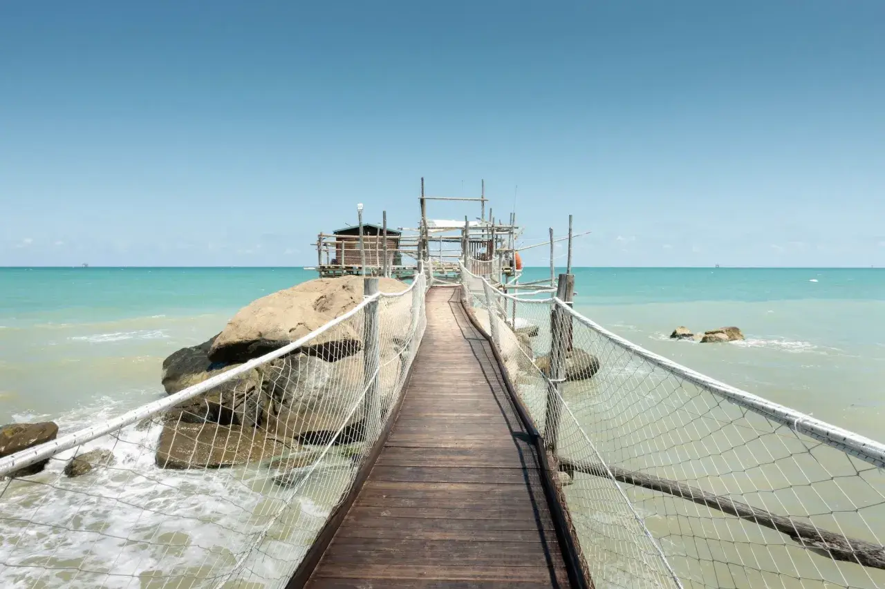 Ponte in legno verso un trabucco, tipica struttura da pesca delle Marche, su un mare azzurro e limpido.