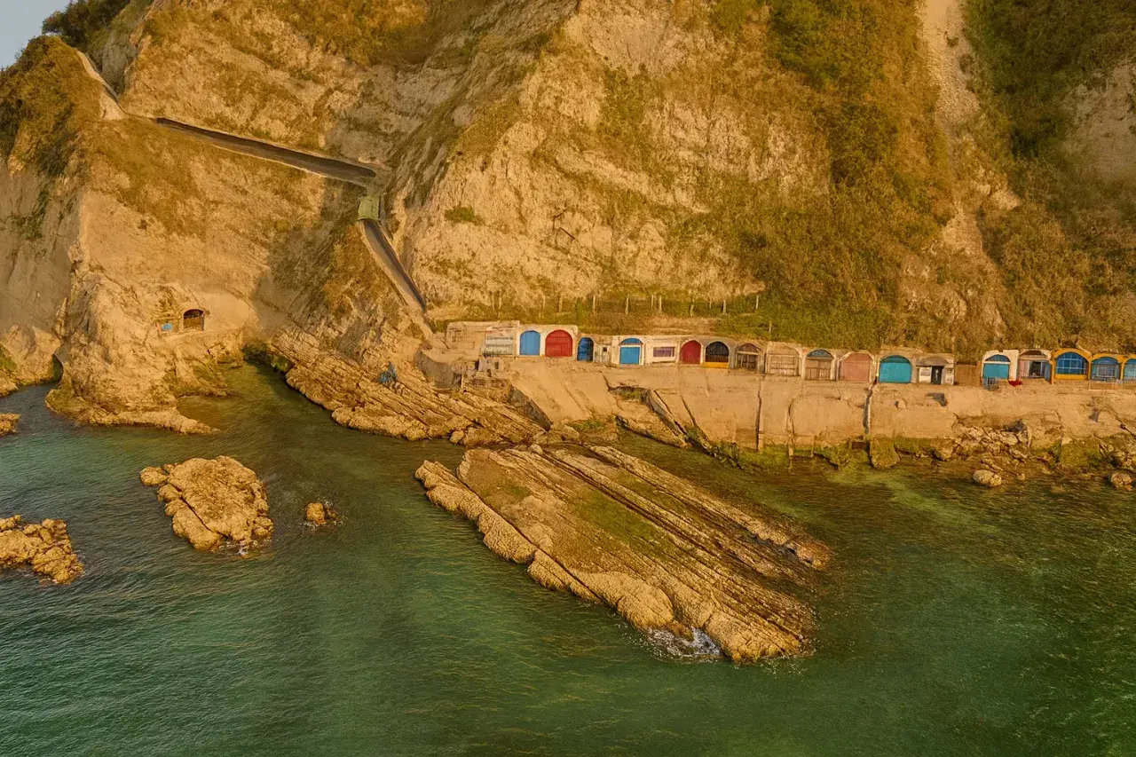 Piccole casette colorate a ridosso della scogliera, con il mare verde smeraldo che lambisce le rocce. Un angolo di paradiso vicino alla grotta azzurra di Ancona.