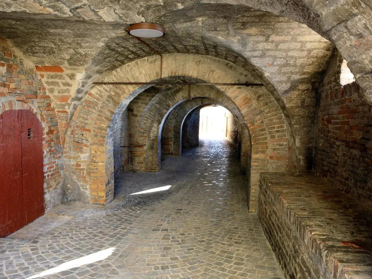 Arco in mattoni a Corinaldo, cosa vedere: un suggestivo passaggio coperto con pavimentazione in pietra e una porta rossa.