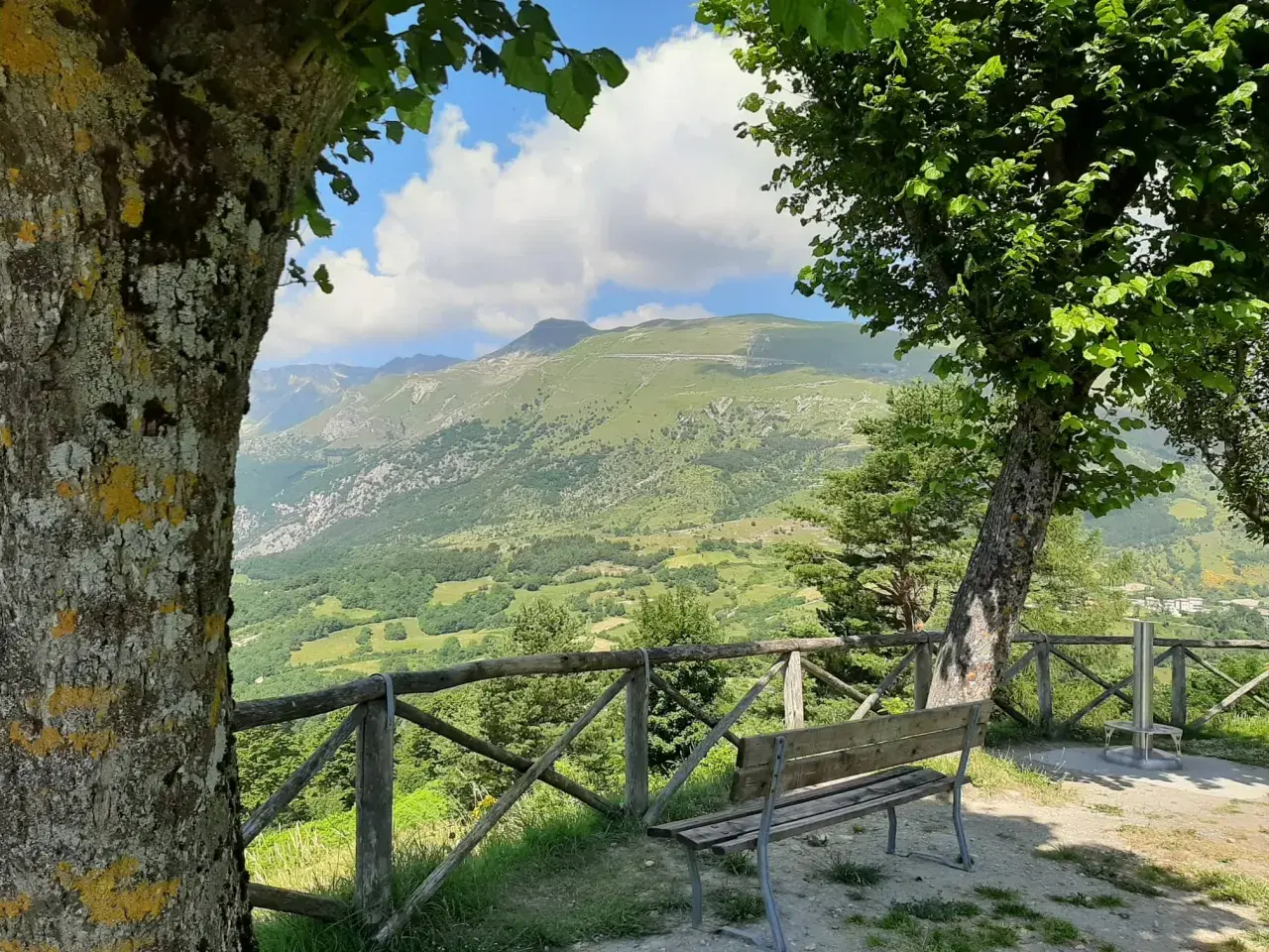 Panoramica mozzafiato del monte Monaco nelle Marche, con un sentiero serpeggiante e un cielo azzurro con nuvole bianche.