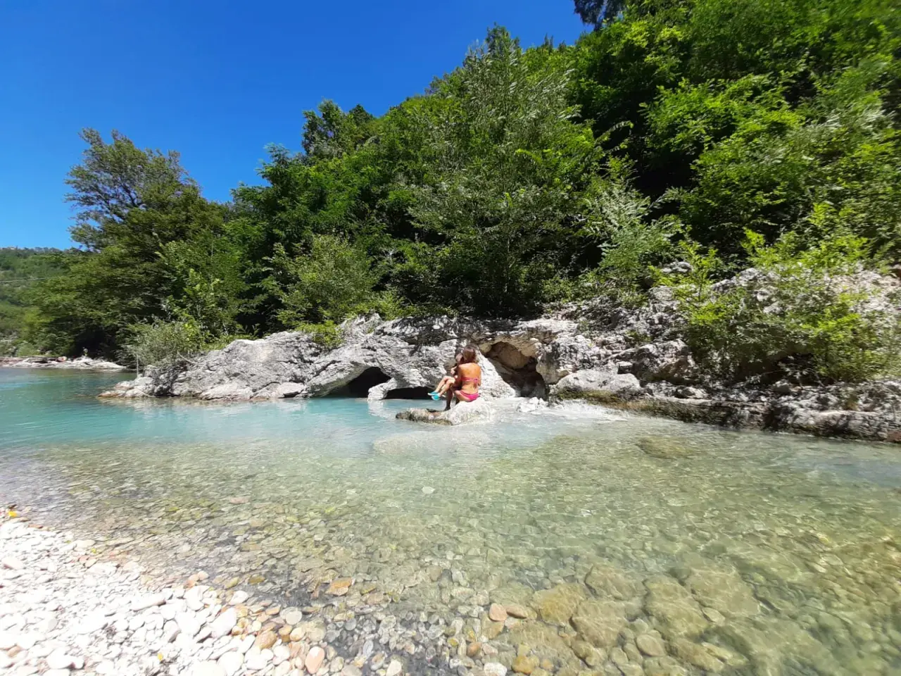 Bambini giocano nel **genga fiume** dalle acque cristalline, circondato da rocce e vegetazione lussureggiante.