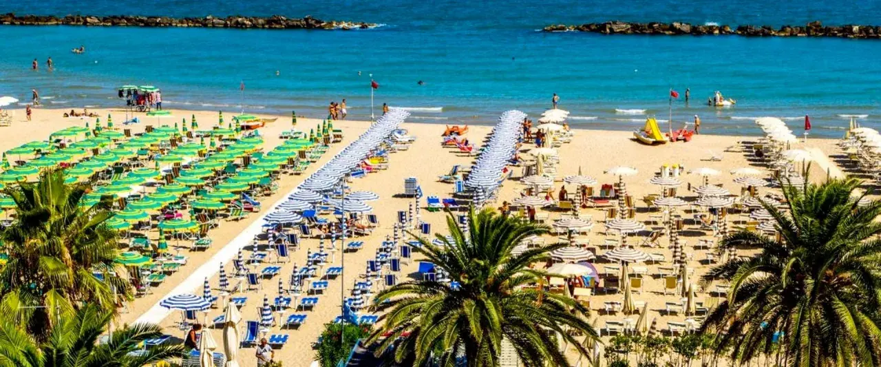 San Benedetto del Tronto: un'ampia spiaggia dorata con file ordinate di ombrelloni verdi e bianchi, lettini e palme. Il mare pulito invita al relax.