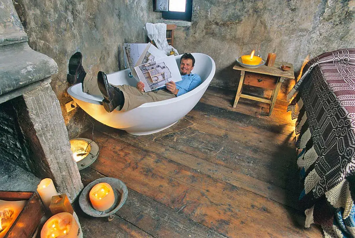 Uomo rilassato in vasca da bagno, legge un libro in un ambiente rustico, forse una casa vacanze a Santo Stefano, Abruzzo, con candele accese.