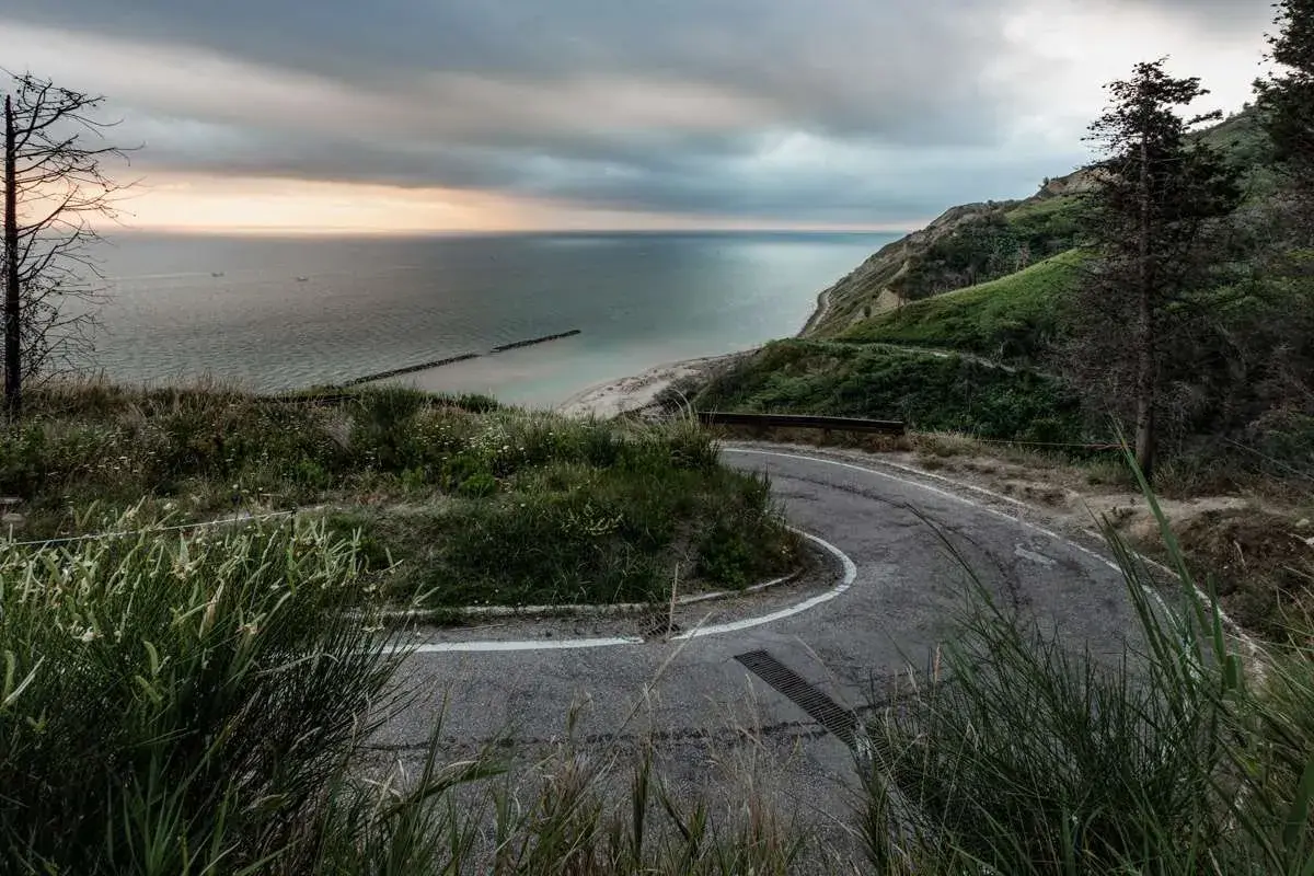 Strada panoramica che sale verso il tetto del mondo a Pesaro, con vista sul mare Adriatico e una costa verdeggiante.