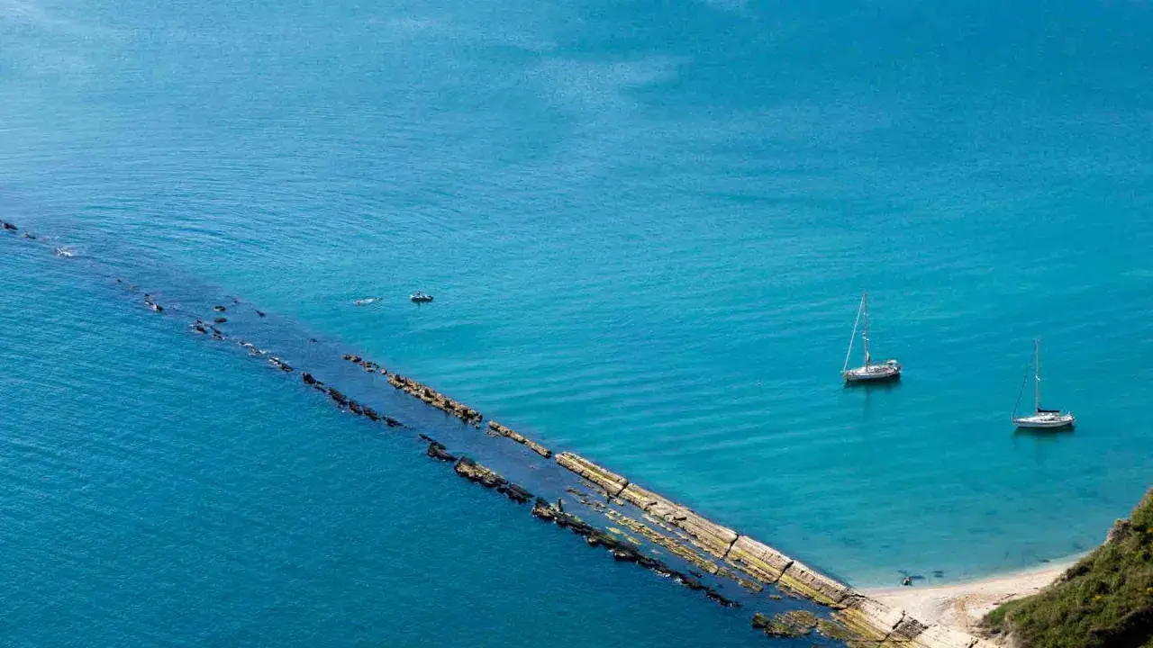 La spiaggia del Trave, con le sue acque cristalline, ospita due barche a vela e un piccolo motoscafo.