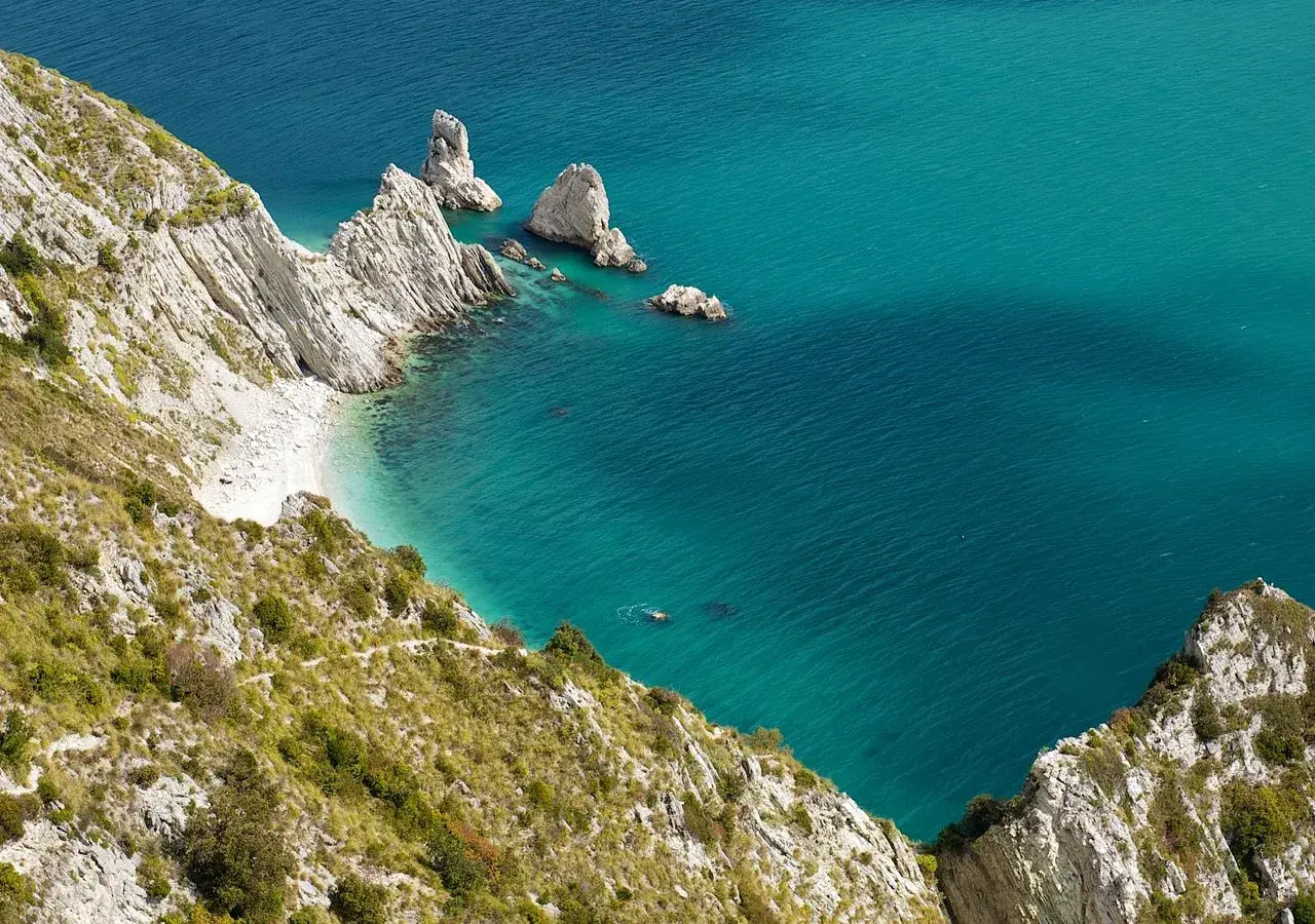 Scogliere bianche e mare cristallino del Conero, con una piccola spiaggia nascosta e un nuotatore solitario.