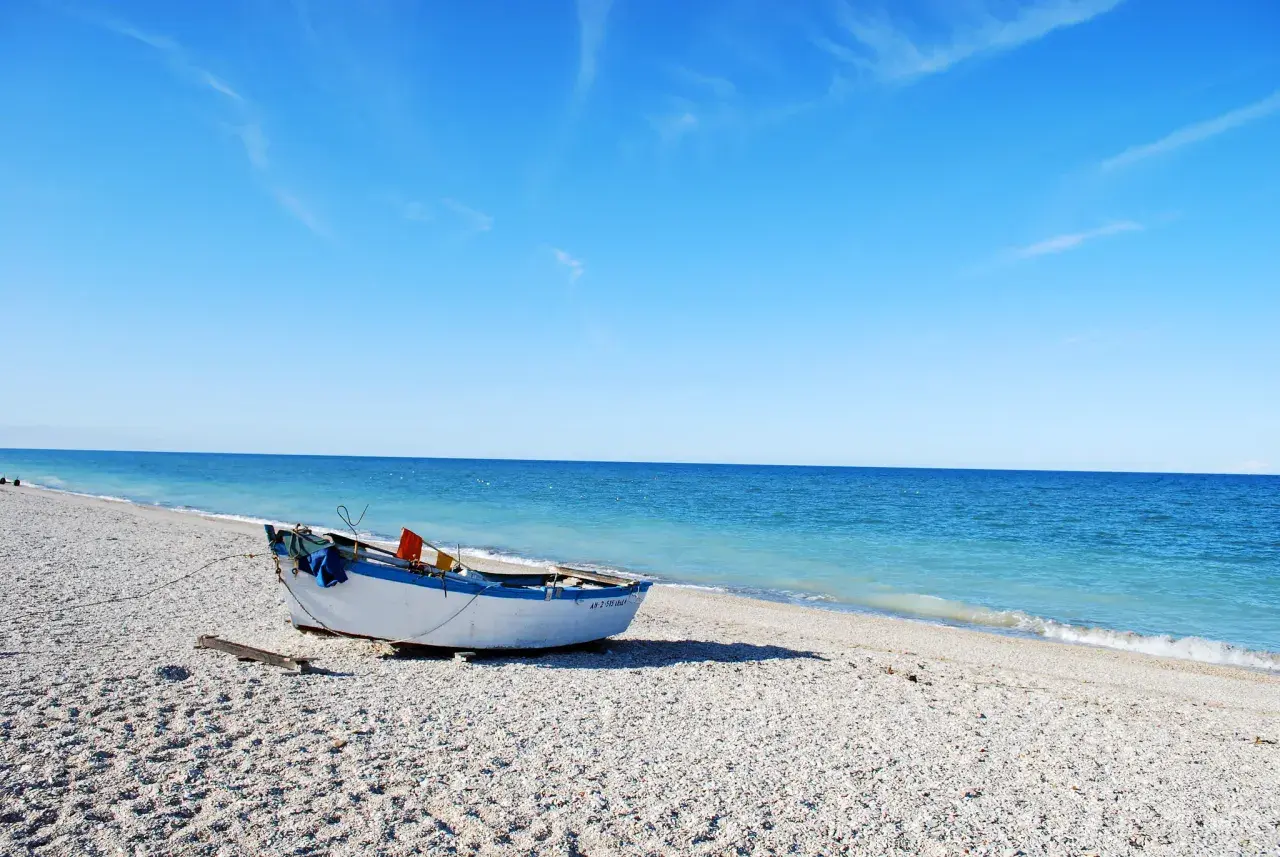 Barca bianca e blu sulla spiaggia di ciottoli a Senigallia, mare calmo e cielo azzurro.