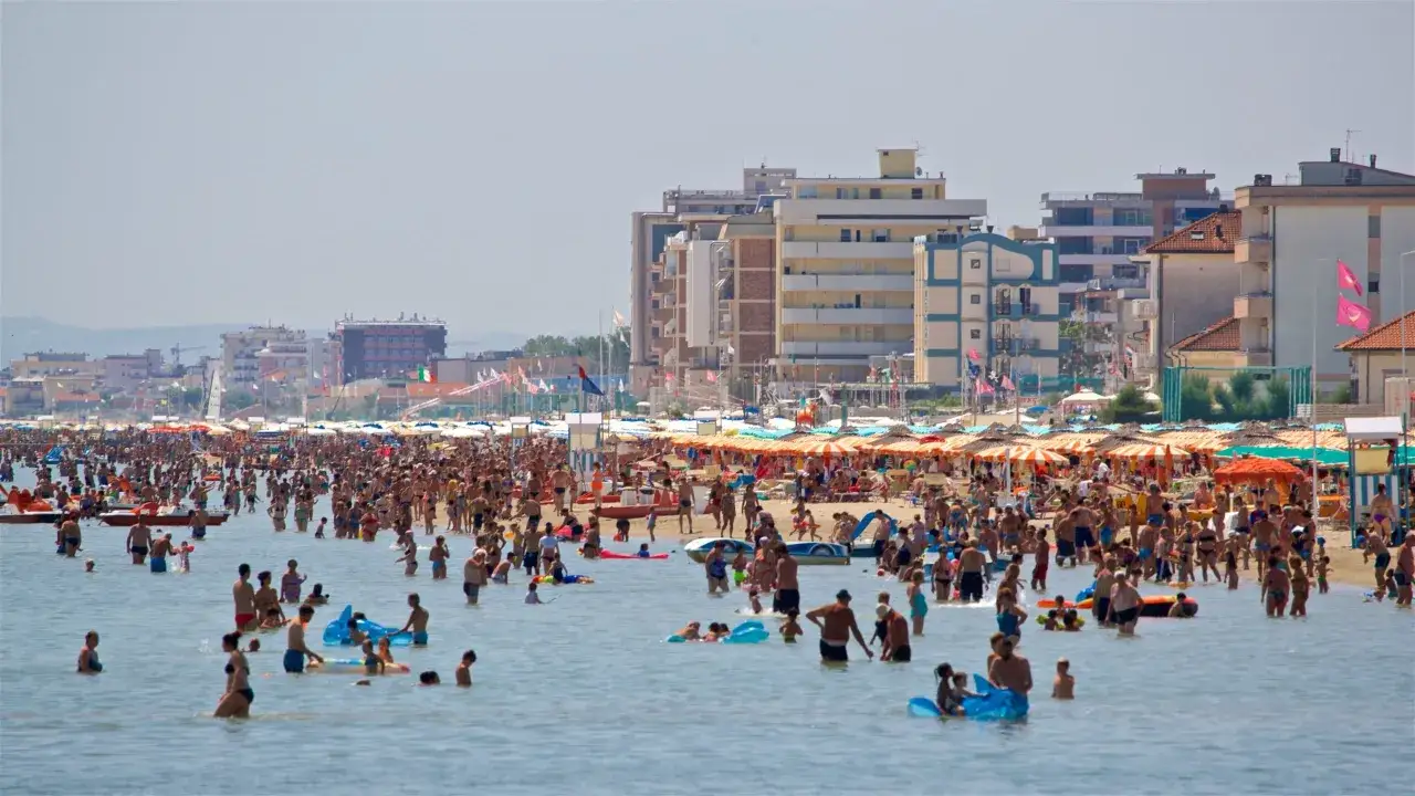 Folla sulla spiaggia e in mare, con ombrelloni colorati e palazzi sullo sfondo. Meglio Bellaria o Igea Marina? Difficile dirlo con tanta gente felice!