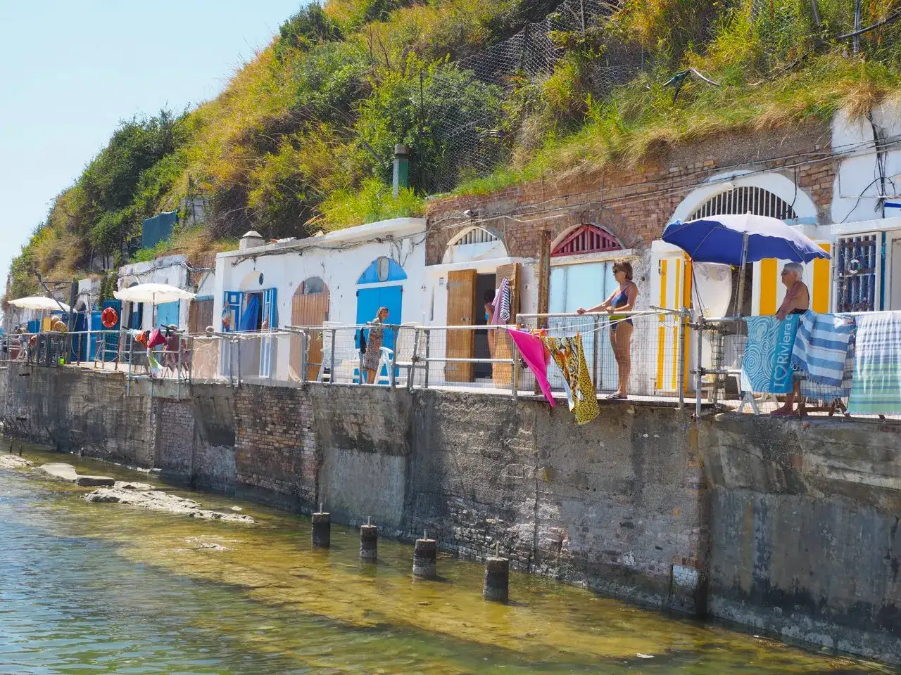 Le cabine colorate della spiaggia del Passetto si affacciano sul mare limpido, con gente che si gode il sole e l'atmosfera estiva.