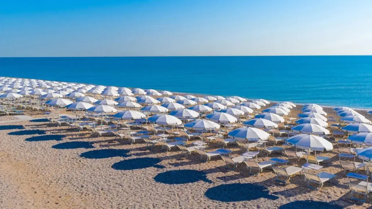 Filettate file di ombrelloni bianchi e lettini sulla spiaggia di Porto San Elpidio, con il mare azzurro sullo sfondo.