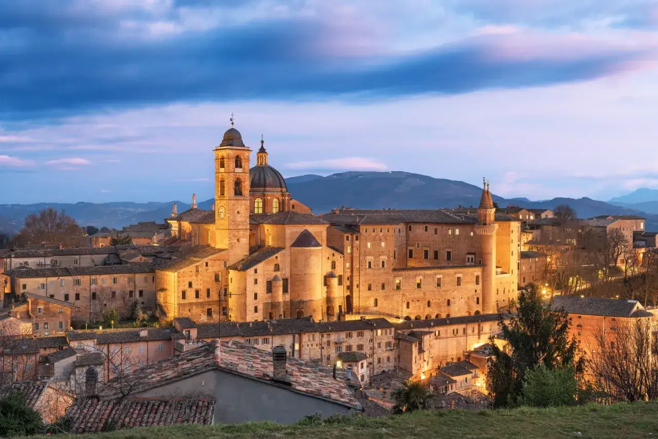 Il Palazzo Ducale di Urbino, gioiello di Pesaro Urbino, brilla al crepuscolo sotto un cielo viola.
