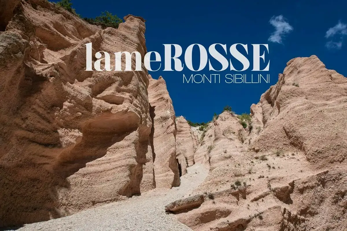 Le lame rosse dei Monti Sibillini, scolpite dal vento, creano un paesaggio surreale sotto il cielo azzurro.