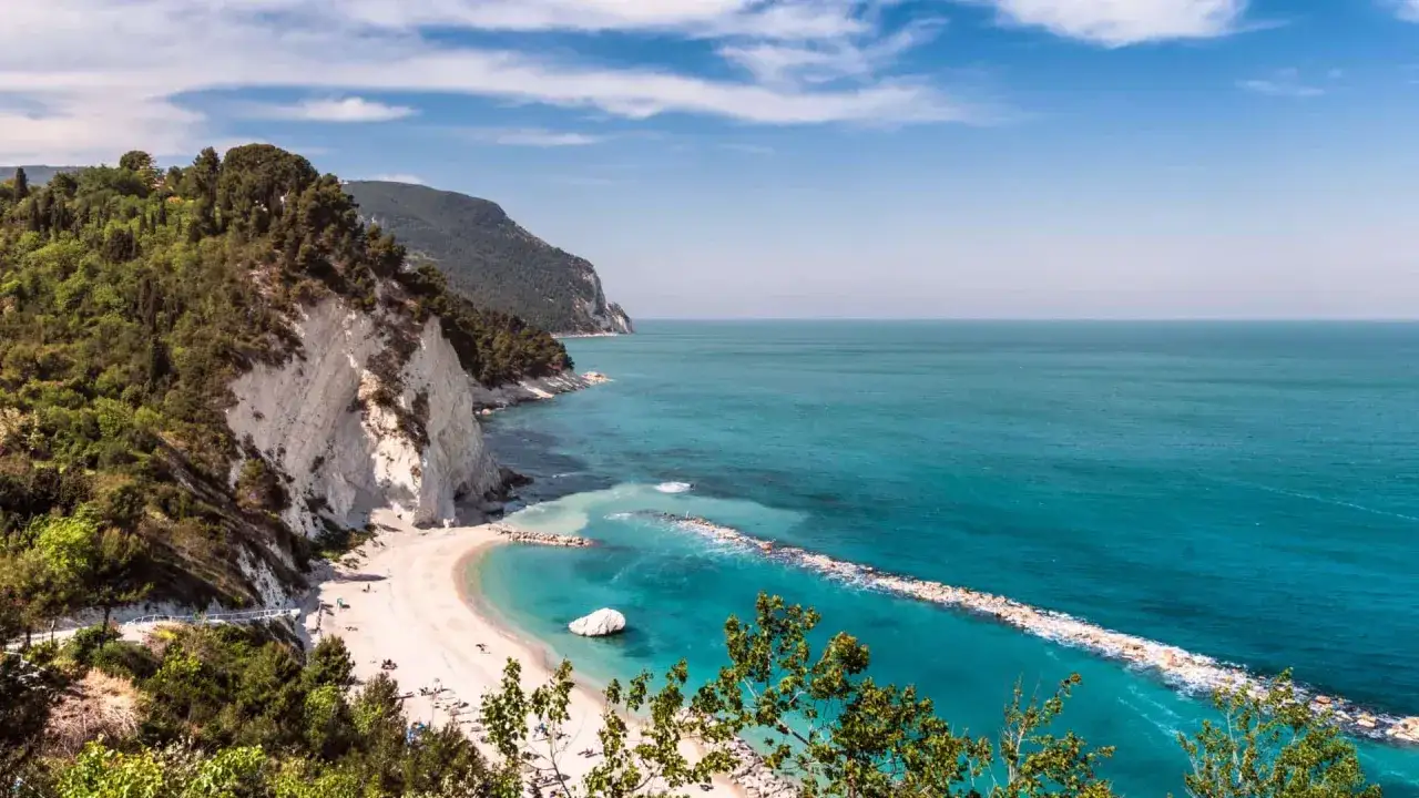 Spiaggia incantevole nel mare Conero, con scogliere bianche, vegetazione lussureggiante e acque cristalline turchesi.