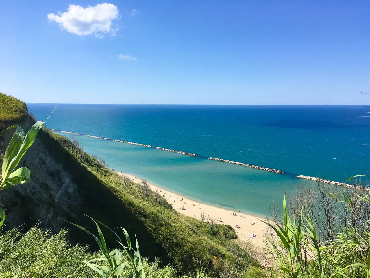 Vista panoramica della spiaggia di Fiorenzuola di Focara, vicino Pesaro, con mare azzurro e scogliera verde.