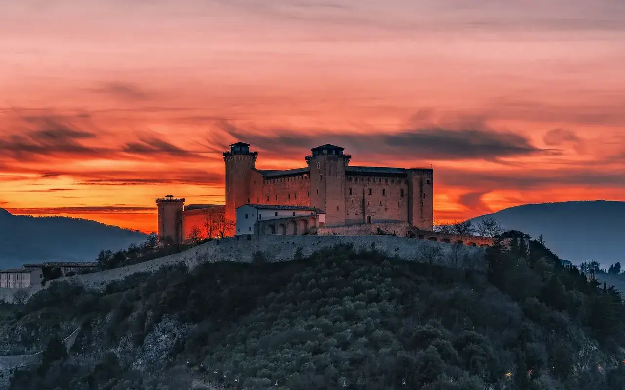 Rocche imponenti su una collina, illuminate da un tramonto infuocato. Questo &egrave; il panorama che ti accoglie se ti chiedi dove si trova Spoleto.