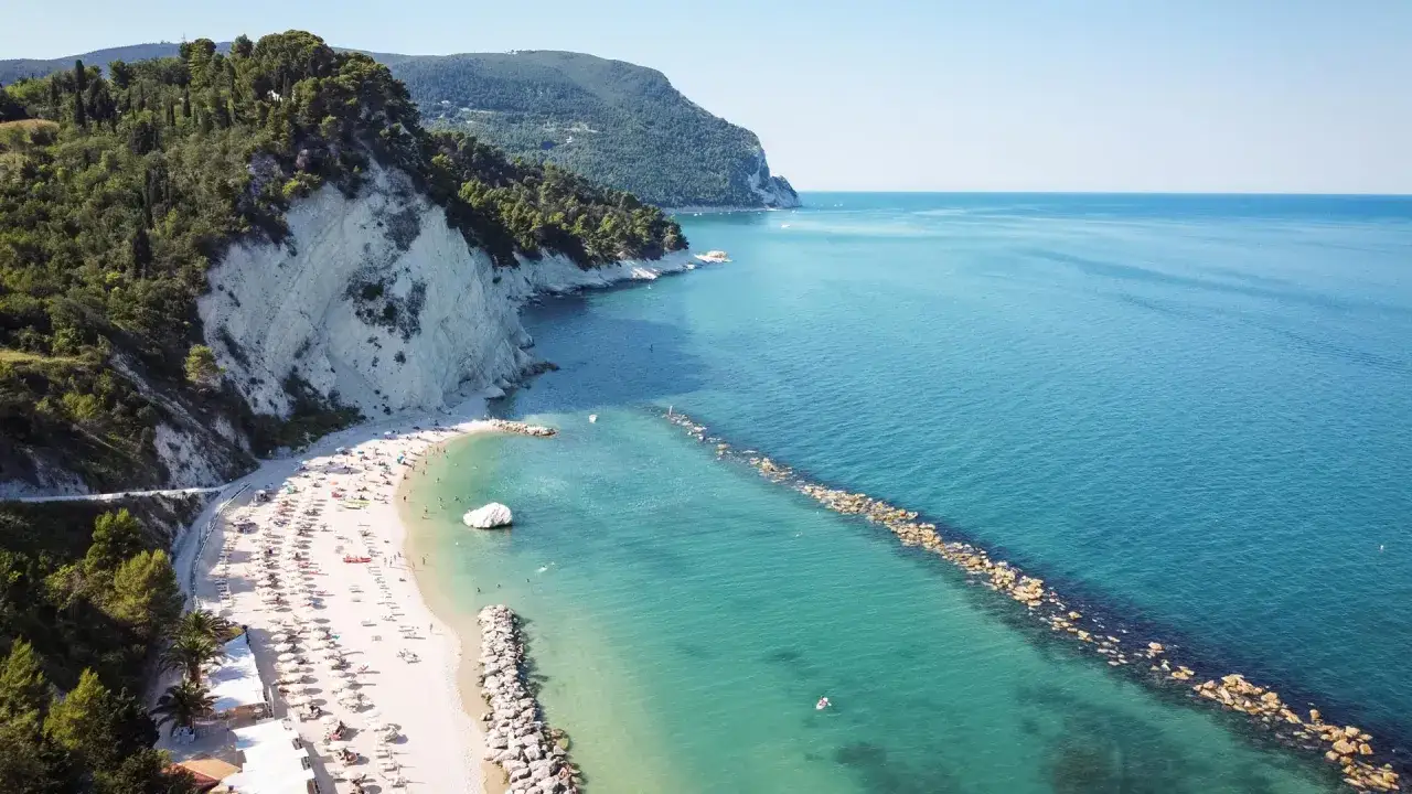 Spiaggia di Cupra Marittima con scogliere bianche e mare cristallino, bagnanti che si godono il sole e le acque turchesi.