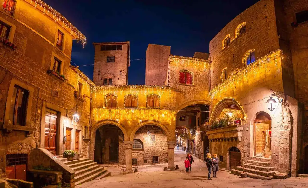 Suggestioni per cosa fare a Viterbo la sera: un vicolo medievale illuminato da lucine natalizie, con archi e palazzi in pietra.