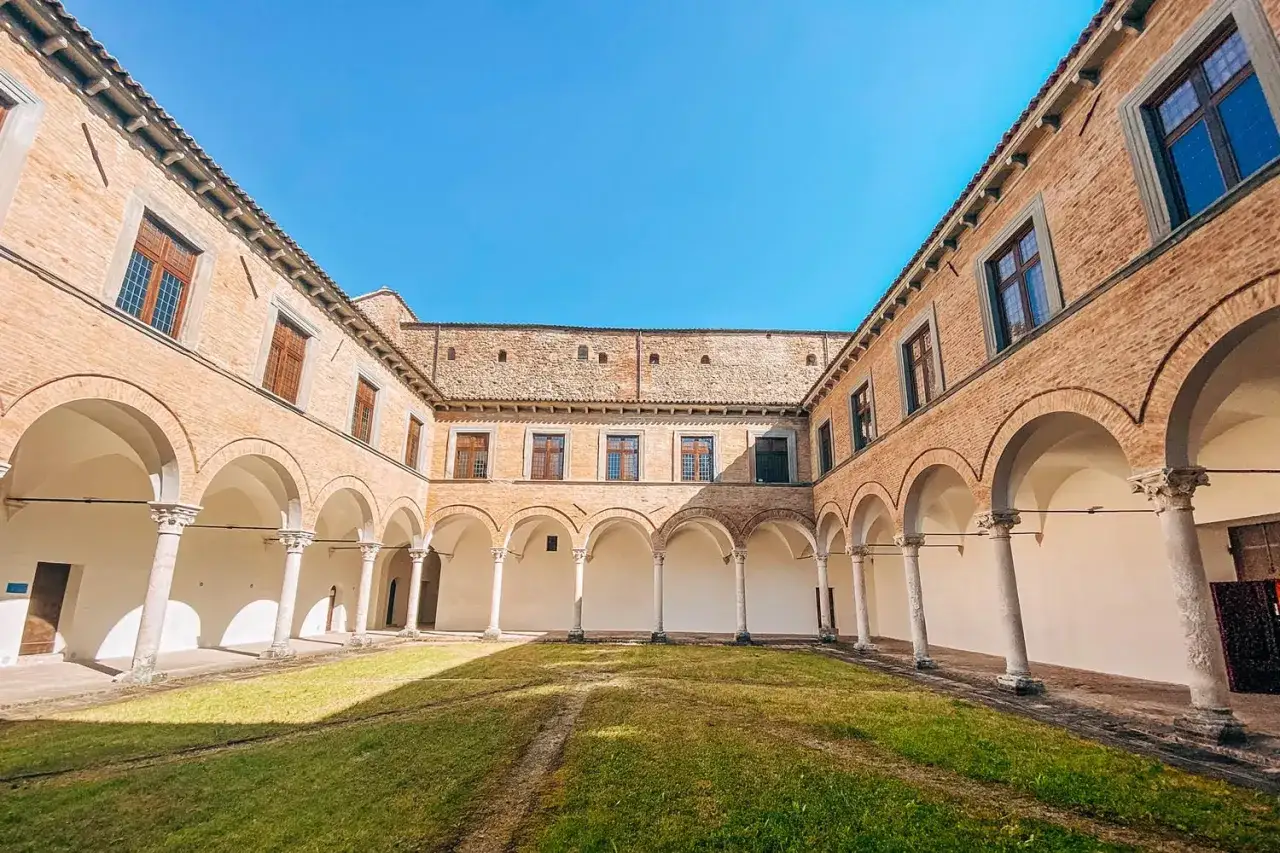 Cortile con portico ad archi e colonne, un prato verde al centro. Un luogo da scoprire tra le cose da vedere a Urbania.