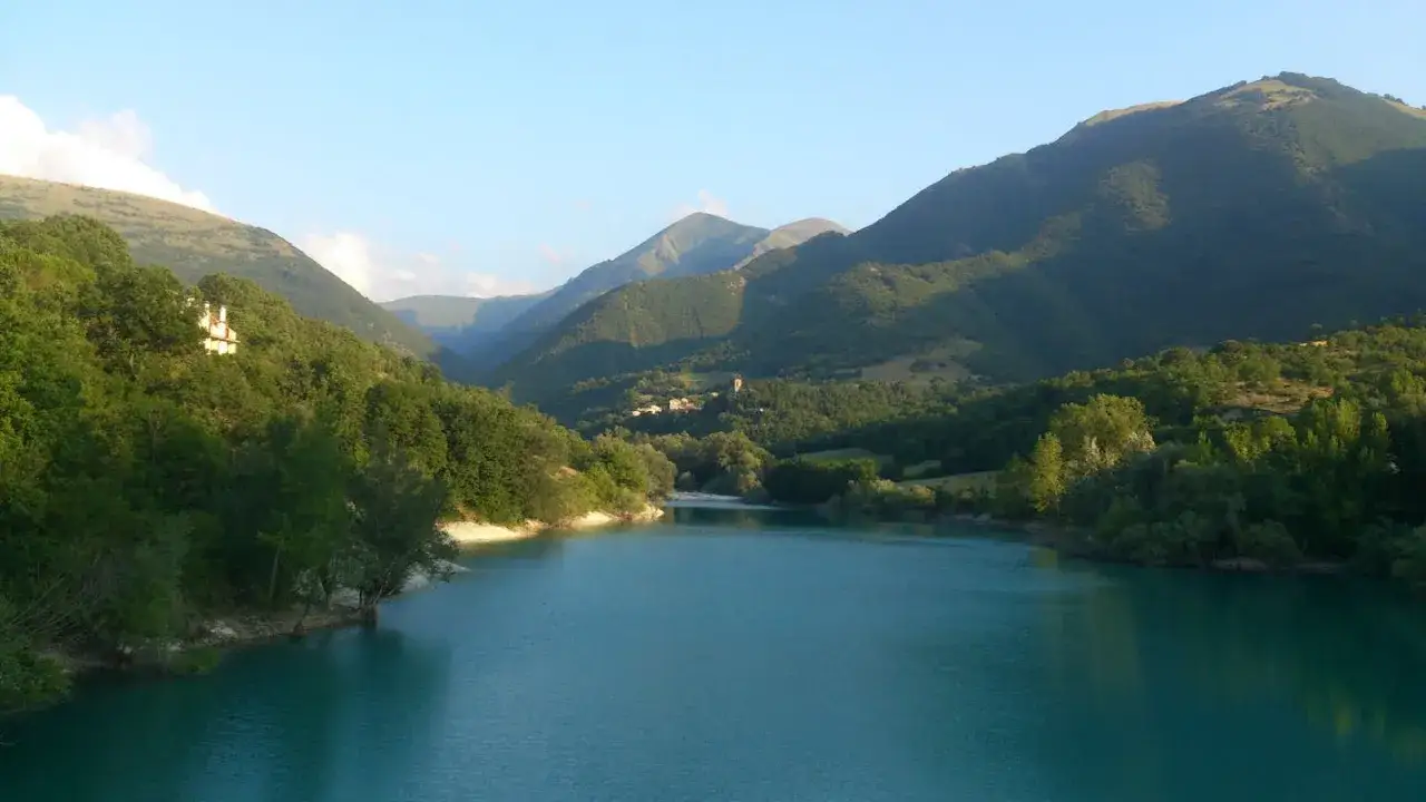 Splendido lago di Fiastra, con montagne verdi e un borgo in lontananza. Cosa vedere? Natura e pace.