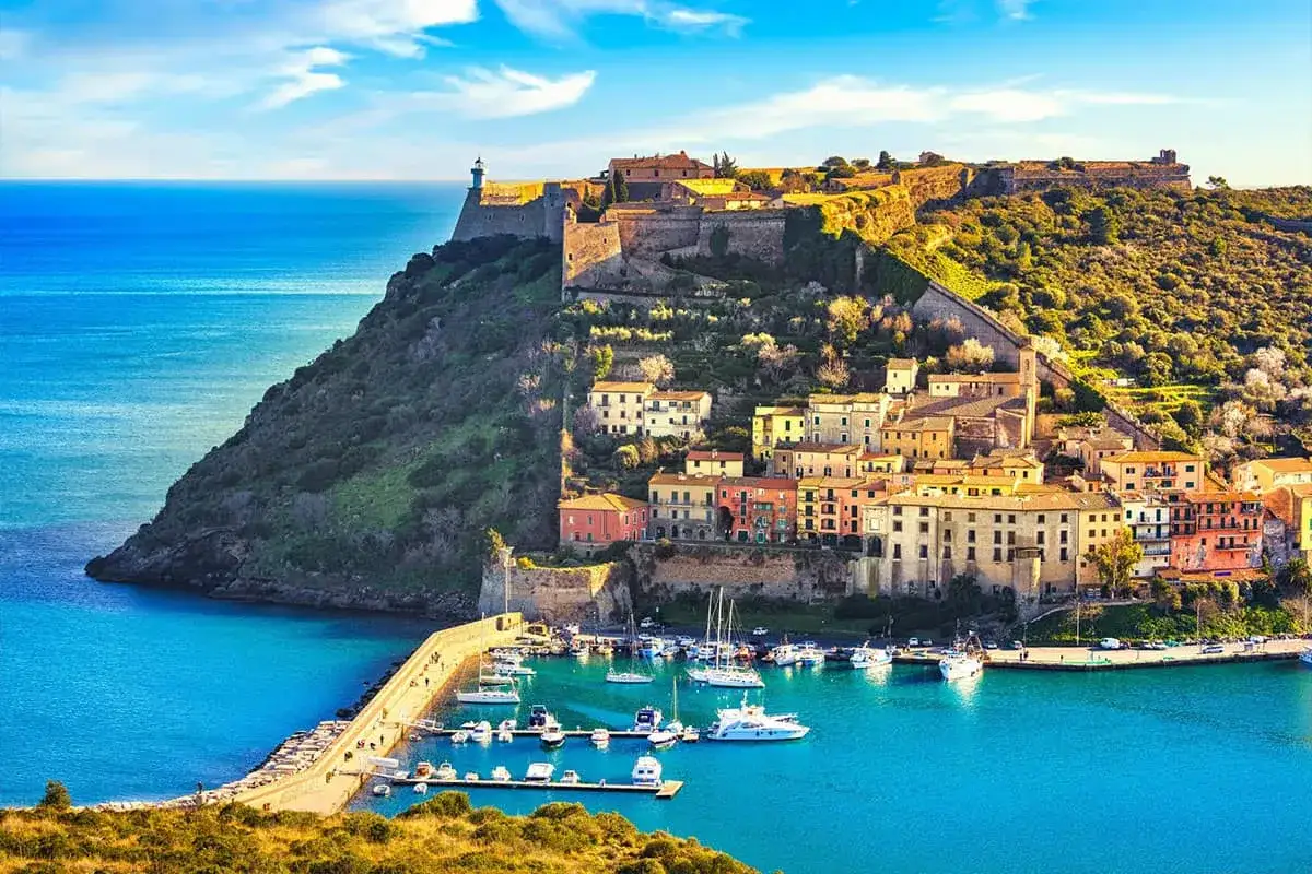 Borgo fortificato sulla costa della marche toscana, con case colorate affacciate su un porto pieno di barche.