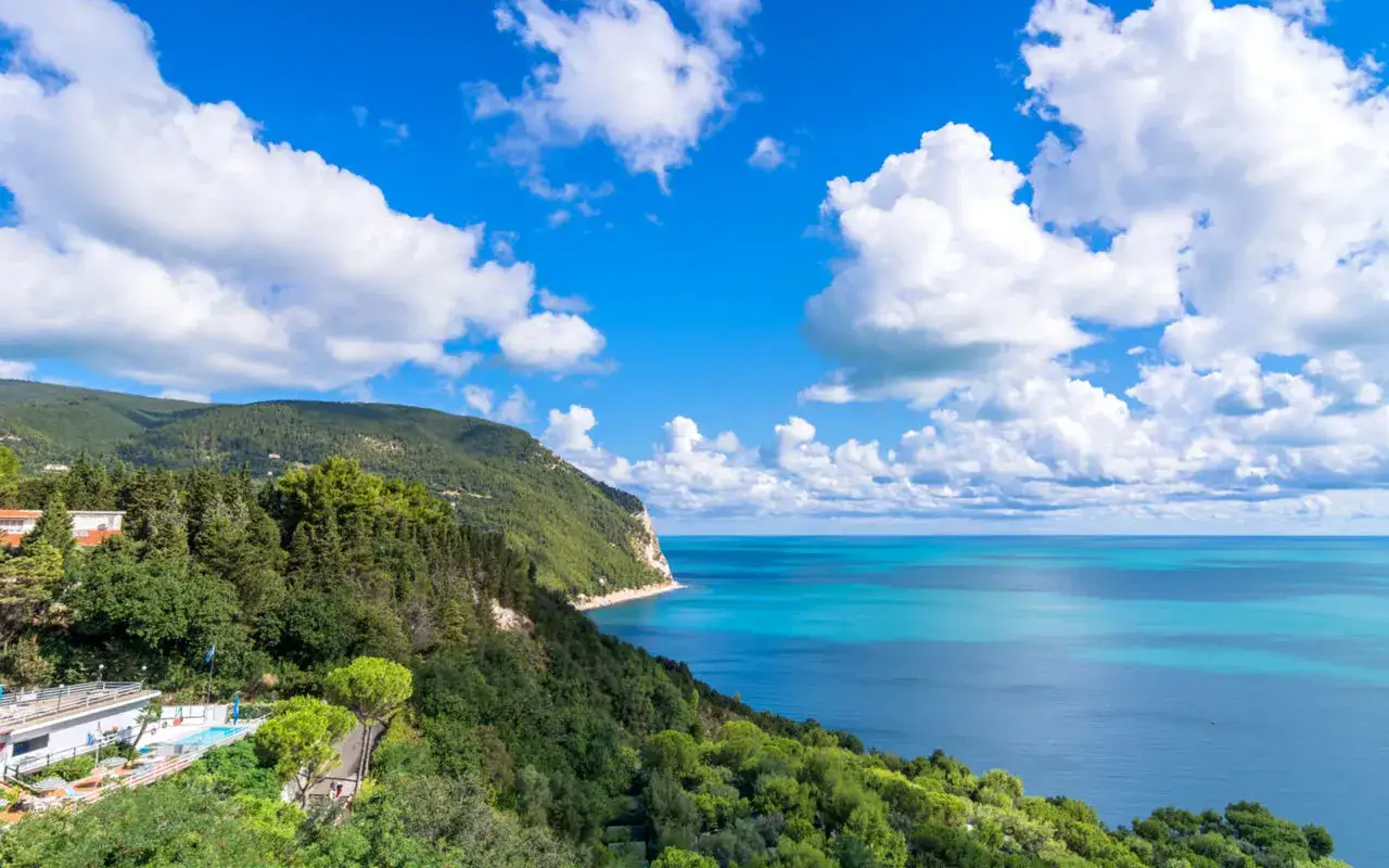 Splendido paesaggio delle Marche: costa verdeggiante, mare azzurro e cielo con nuvole bianche.