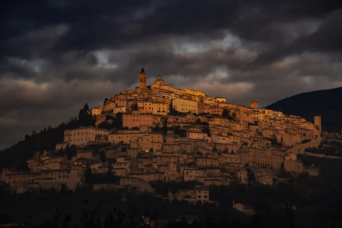 Borgo medievale illuminato al tramonto, con torri e chiese che spiccano tra le case arroccate. Un luogo magico dove scoprire cosa vedere a Trevi.