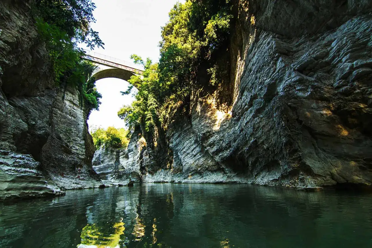 Gola con acqua verde e un ponte ad arco, che ricorda le marmitte dei giganti nelle Marche.
