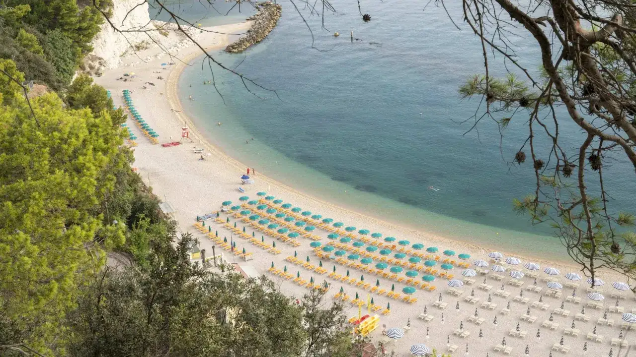 Vista dall'alto della spiaggia San Michele a Sirolo, con file ordinate di ombrelloni verdi e lettini gialli che si estendono lungo la costa.