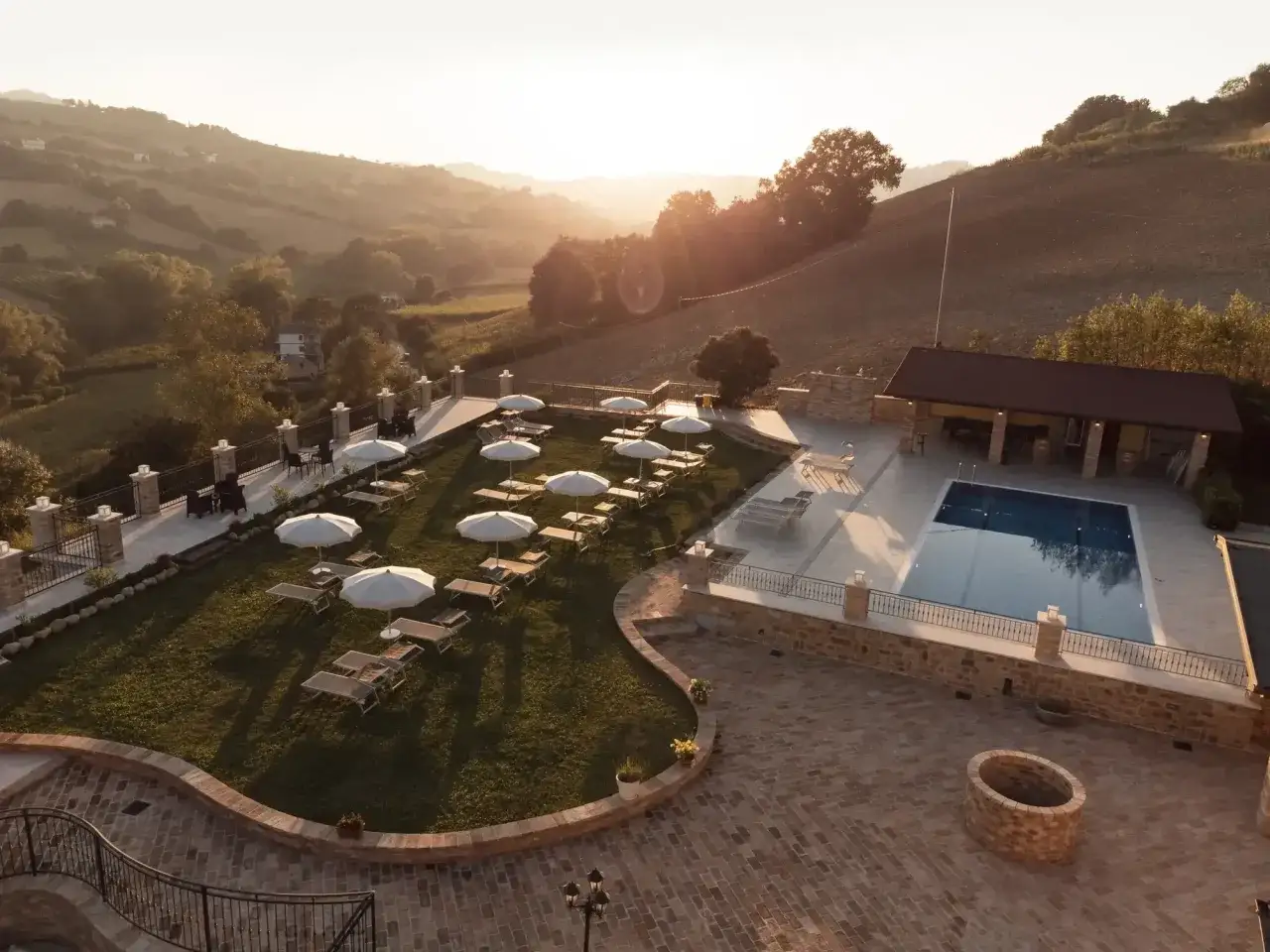 Piscina e lettini in un resort di lusso nelle Marche, con dolci colline sullo sfondo al tramonto. Un'oasi di relax per la tua spa.