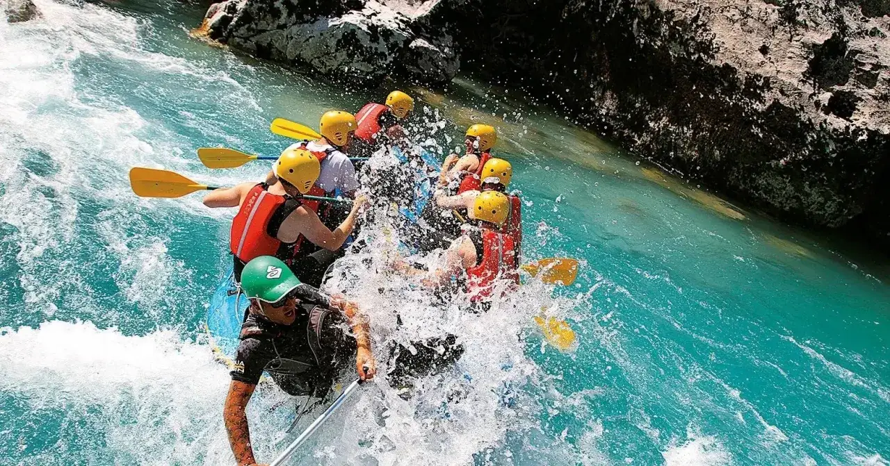 Un gruppo di persone si diverte con il rafting nelle Marche, pagaiando su acque turchesi tra rocce scure.
