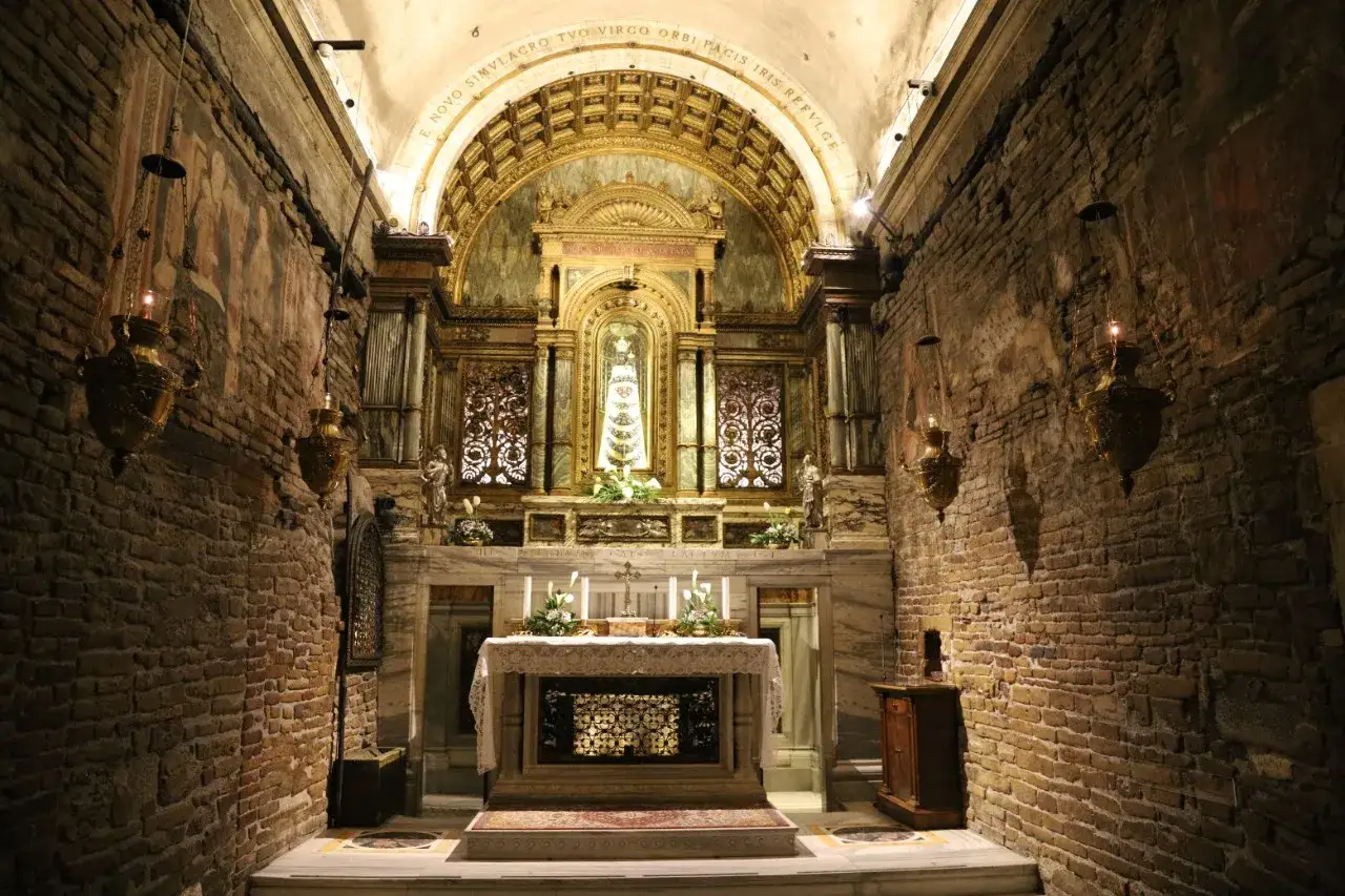 Interno di una cappella con un altare ornato e una statua della Madonna di Loreto. Pareti in mattoni a vista e lampade dorate creano un'atmosfera suggestiva.