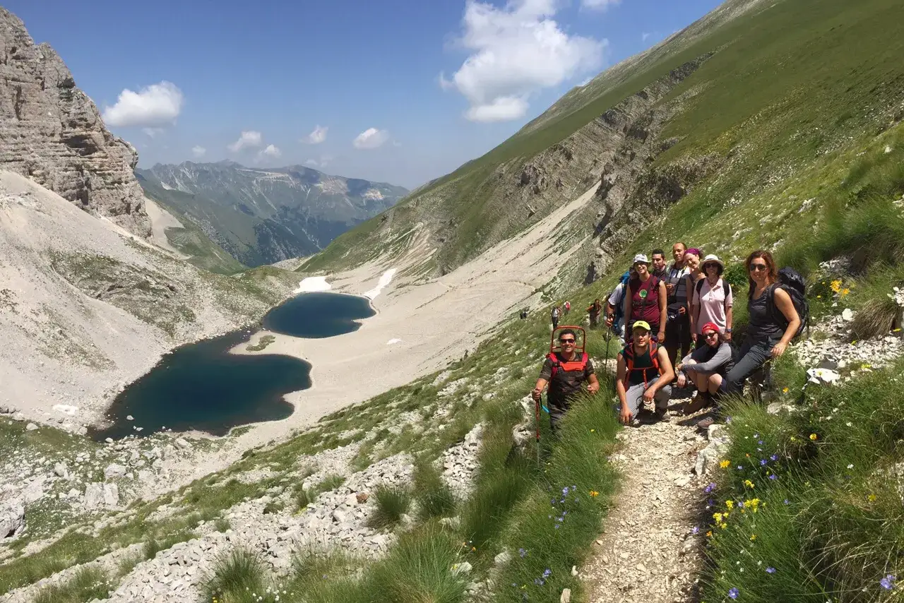 Un gruppo di escursionisti sui sentieri dei Monti Sibillini, con laghi alpini e montagne sullo sfondo.