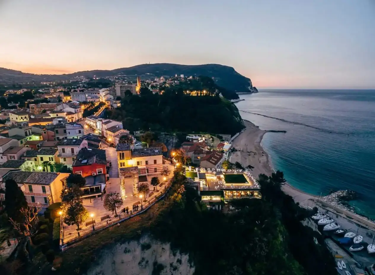 Luci accese nel centro di Numana, con il mare calmo e la spiaggia che si estende verso il promontorio.