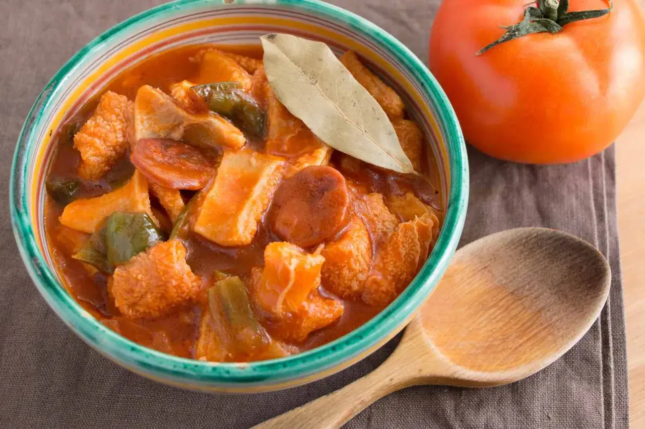 Un invitante piatto di trippa alla marchigiana, con peperoni e pomodoro, pronto per essere gustato con un cucchiaio di legno.