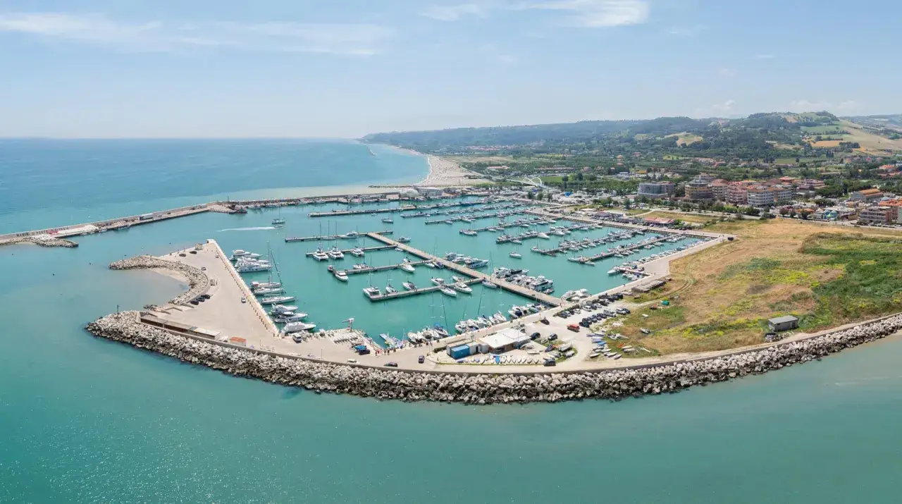 Vista aerea del porto turistico di Porto San Giorgio, con numerose imbarcazioni ormeggiate e la costa sullo sfondo.