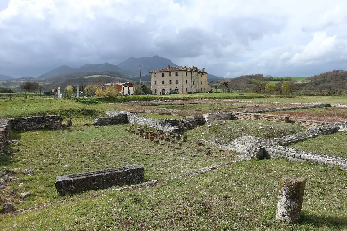Rovine antiche e un edificio giallo sullo sfondo. Sassoferrato cosa vedere: un sito archeologico immerso nel verde.