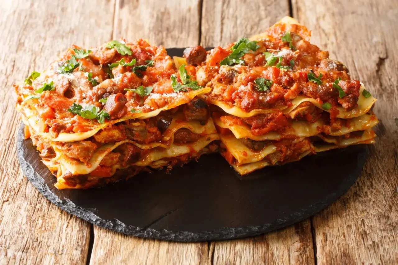 Lasagne ricche e saporite, un classico tra i piatti tipici delle Marche, servite su una pietra scura.