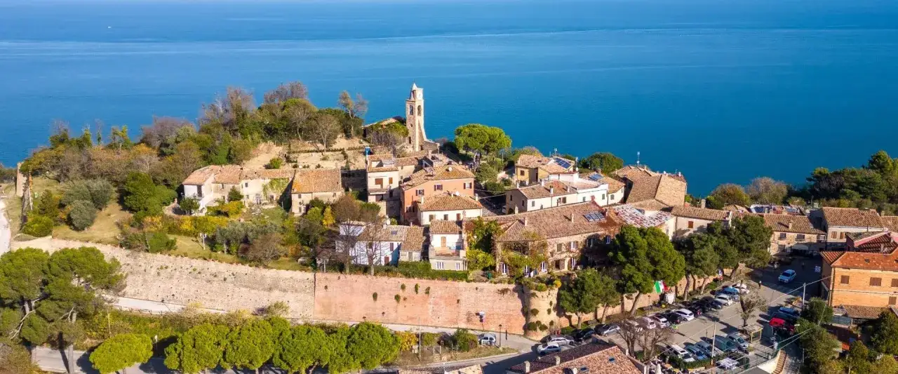 Borgo medievale di Gabicce Mare cosa vedere: un panorama mozzafiato sul mare Adriatico, con case in pietra, un campanile e vegetazione rigogliosa.