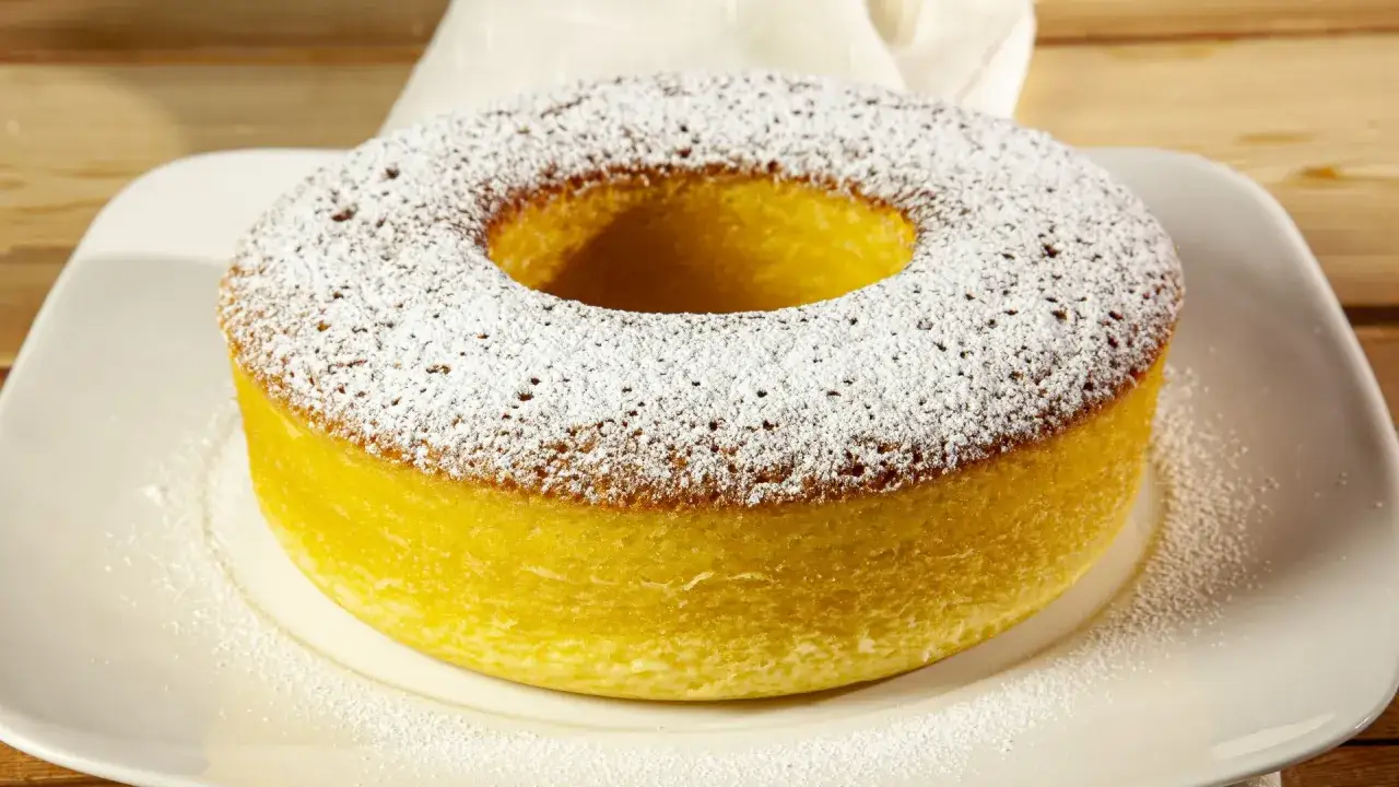 Ciambellone marchigiano ricetta originale, soffice e dorato, spolverato di zucchero a velo su un piatto bianco.