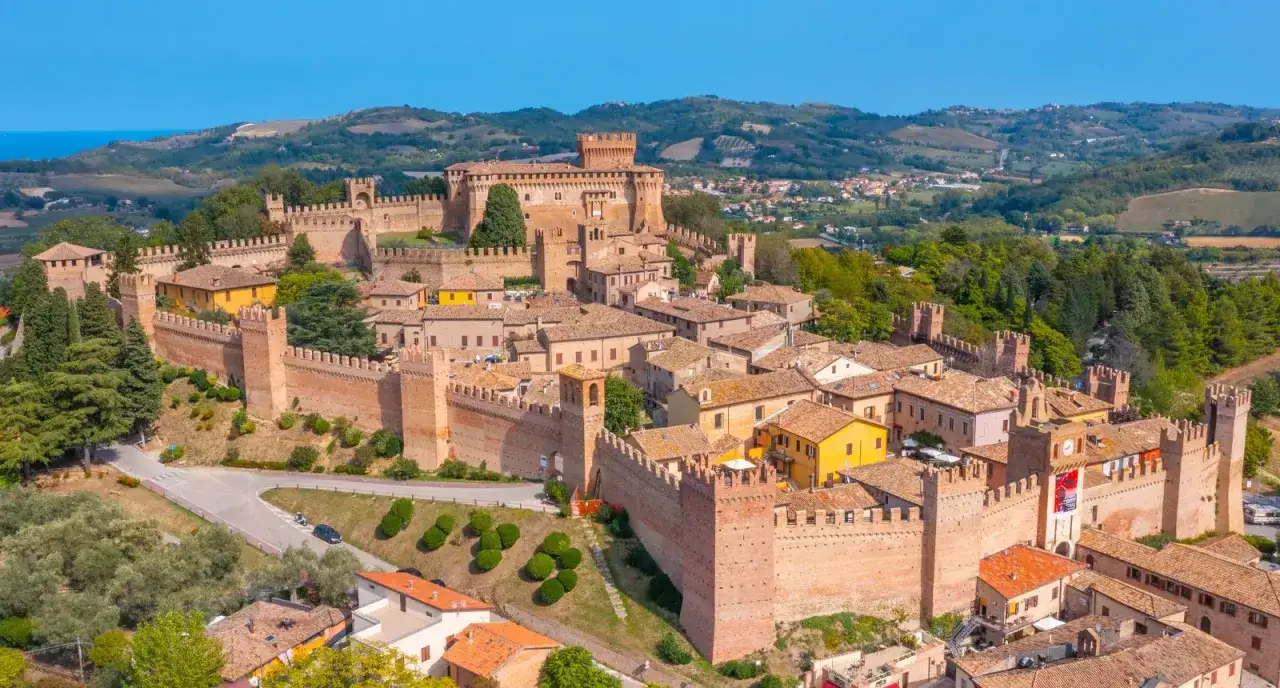 Borgo medievale fortificato nelle Marche, con mura imponenti, torri e case con tetti rossi.